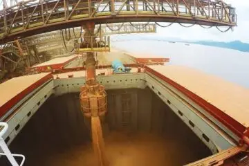 Imagem representa exportação do agro. Grãos sendo descarregados em um navio.